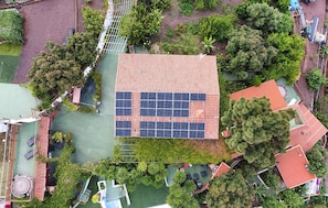 Vista aèria d'un edifici amb una instal·lació de panells solars a la teulada, envoltat de vegetació i una pista de tennis.