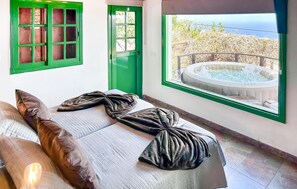 Habitació amb llit, finestra que ofereix vistes a una banyera hidromassatge i un balcó, i finestres amb marc verd.