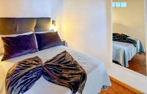 Un lit bien fait, avec une grande couverture épaisse de couleur sombre, une tête de lit et une lampe de chevet.