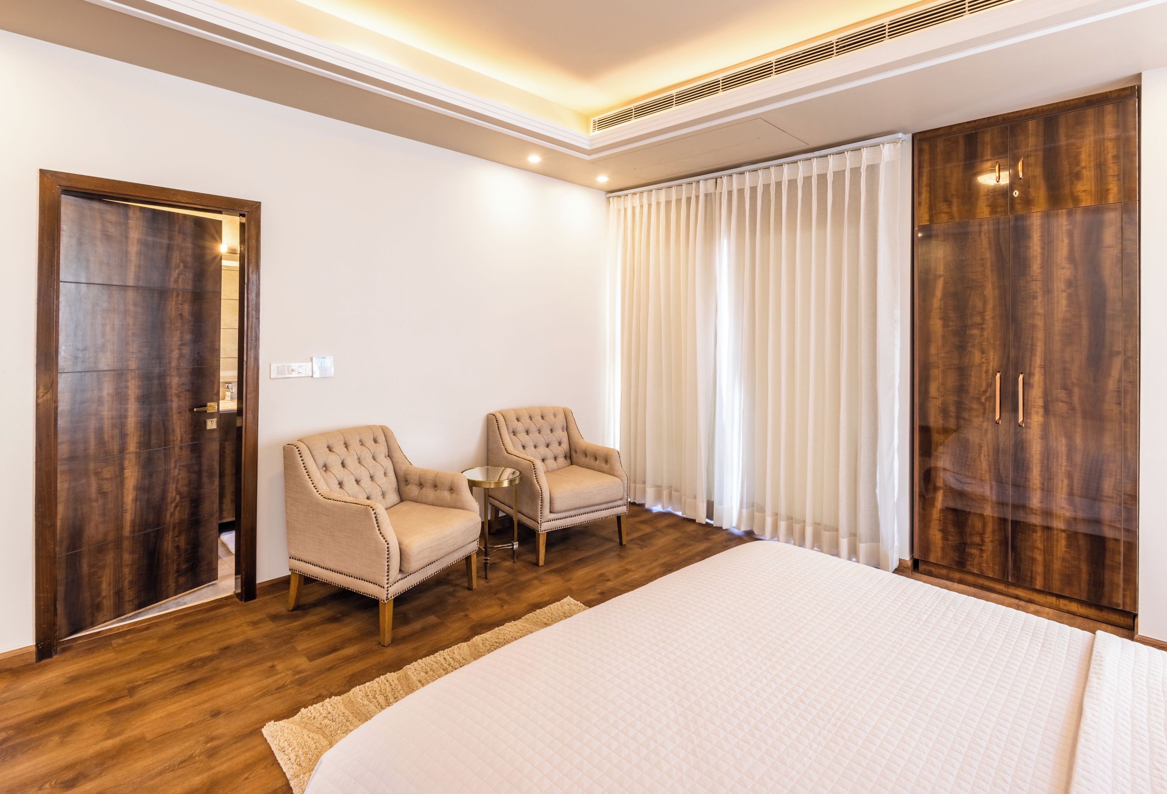 Una habitación de hotel con una cama grande, dos sillones, una mesita, un armario y una ventana con cortinas.