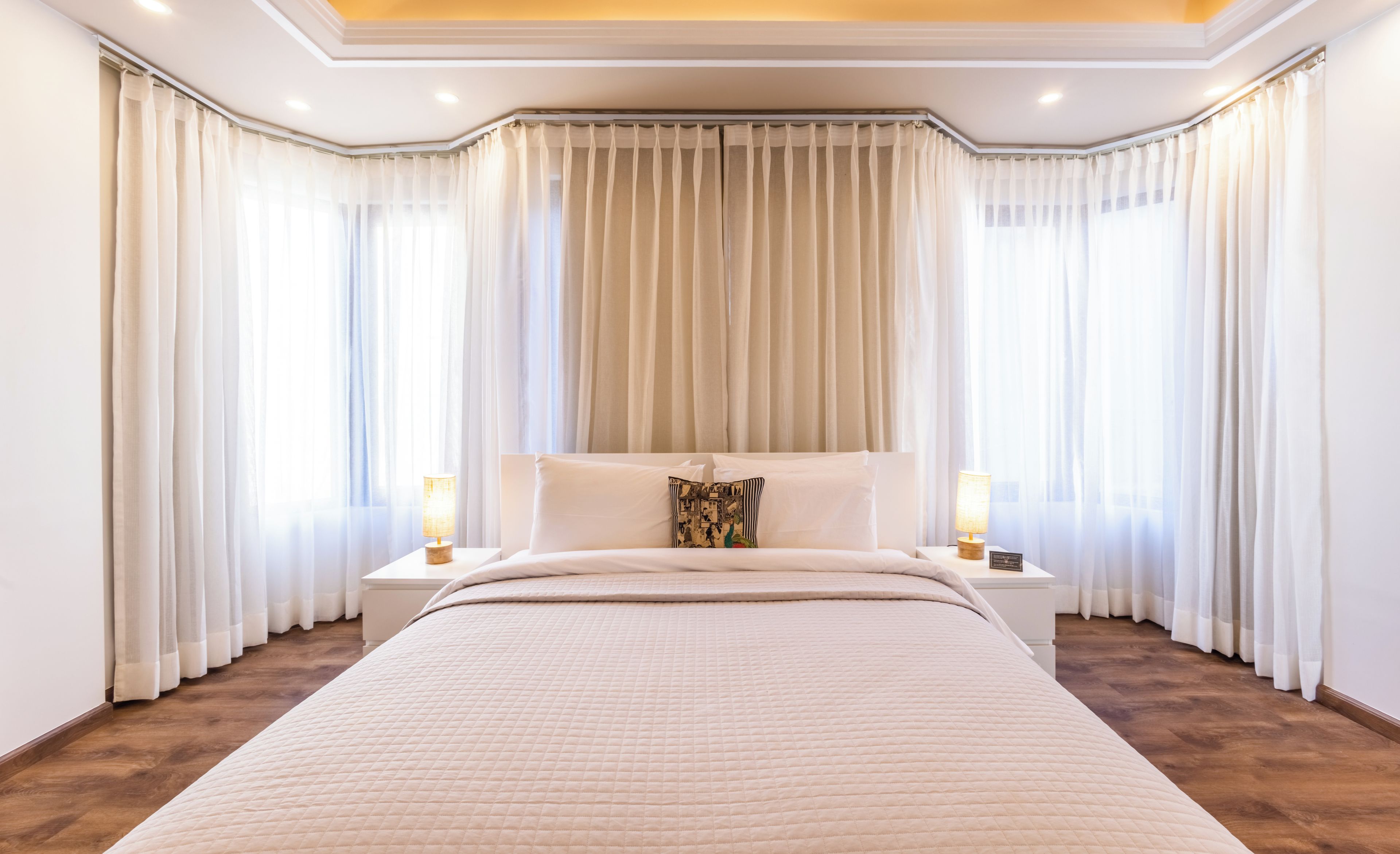 A hotel room with a large bed, two bedside tables with lamps, and a view of the outdoors through sheer curtains.