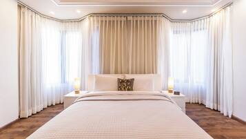 A hotel room with a large bed, two bedside tables with lamps, and a view of the outdoors through sheer curtains.