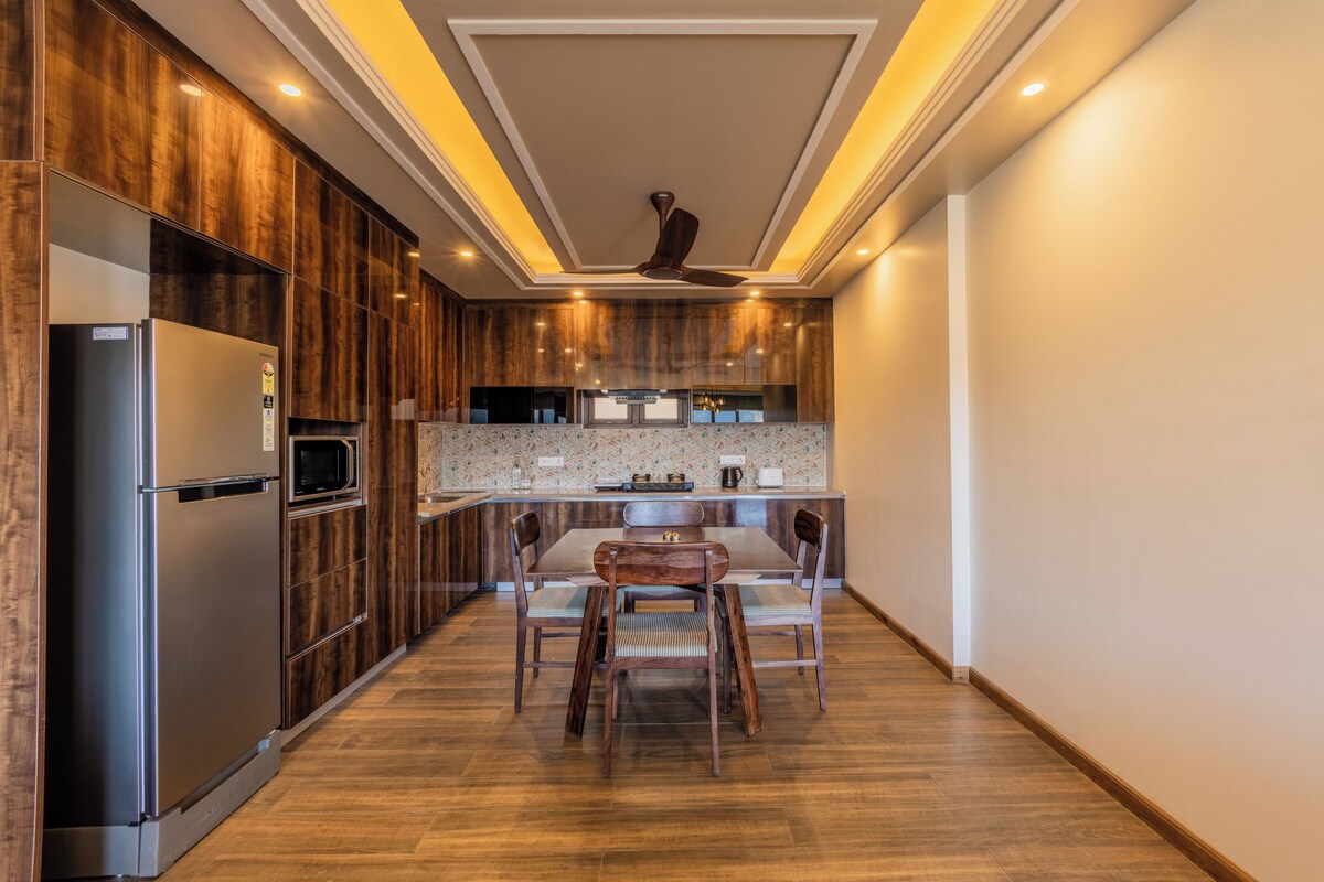 A modern kitchen with a built-in microwave, a stainless steel refrigerator, wooden cabinetry, and a dining area with a table and chairs.