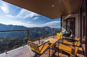 Un balcon doté de meubles en bois, d’un fauteuil suspendu et offrant une vue sur les montagnes.