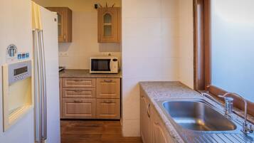 A compact kitchen with wooden cabinets, a built-in microwave, and a stainless steel sink.