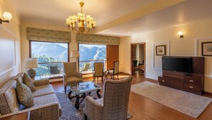 A living room with a sofa, chairs, a coffee table, a TV, and a balcony with a mountain view.