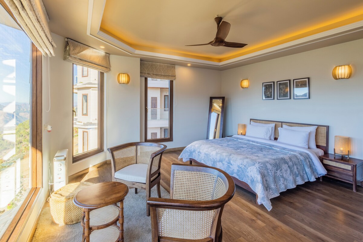 A hotel room with a large bed, a sitting area with chairs, a ceiling fan, and a view of the mountains.