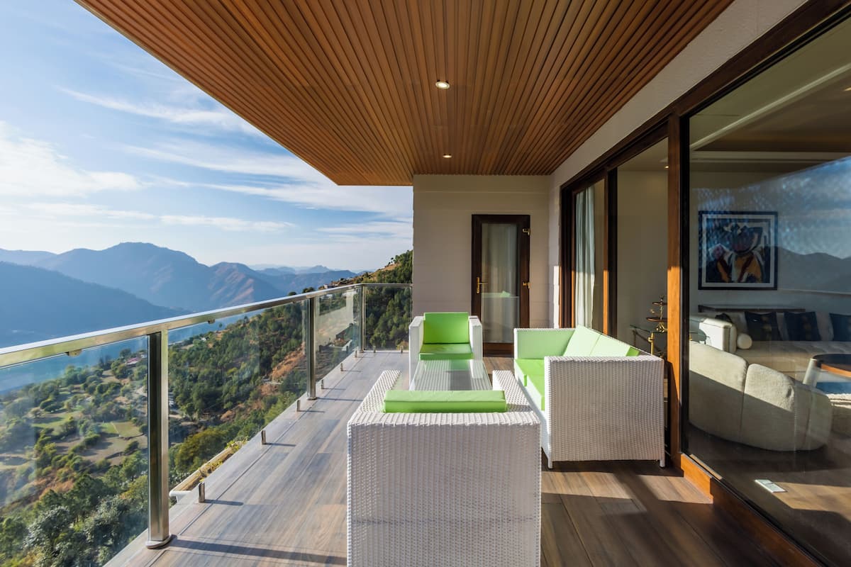 Ein Balkon mit Korbmöbeln, einer Glastrennwand und Blick auf Berge.
