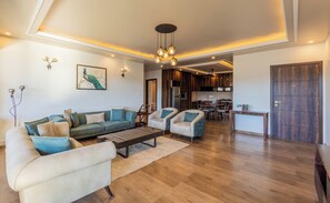 A modern living room with a sofa, armchairs, a coffee table, and a dining area with a kitchen in the background.