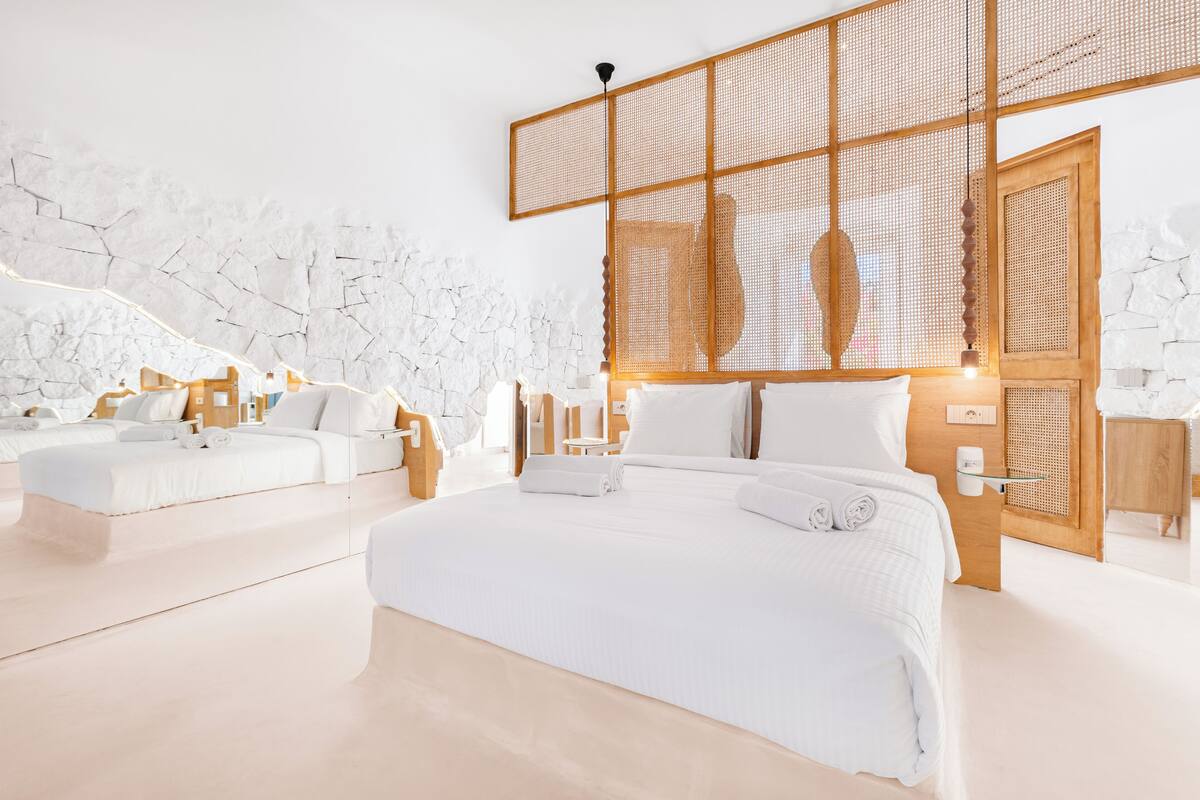 A modern hotel room with a large bed, a smaller sofa, and a wooden partition.
