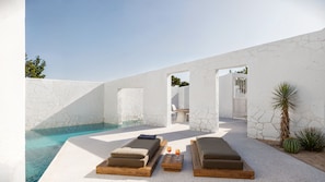 Uma área moderna com piscina ao ar livre, cadeiras de descanso e mesa, cercada por paredes brancas e plantas.