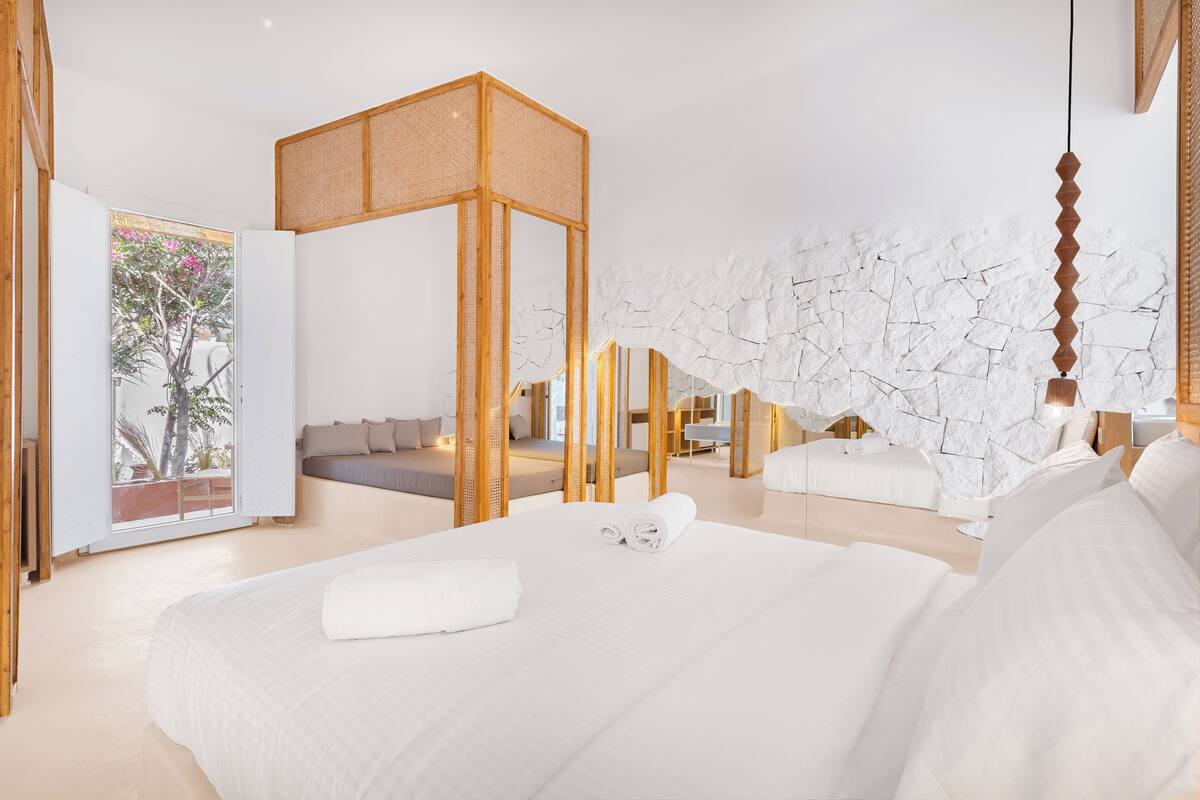 A modern hotel room with a large bed, a wooden partition, and a stone wall.