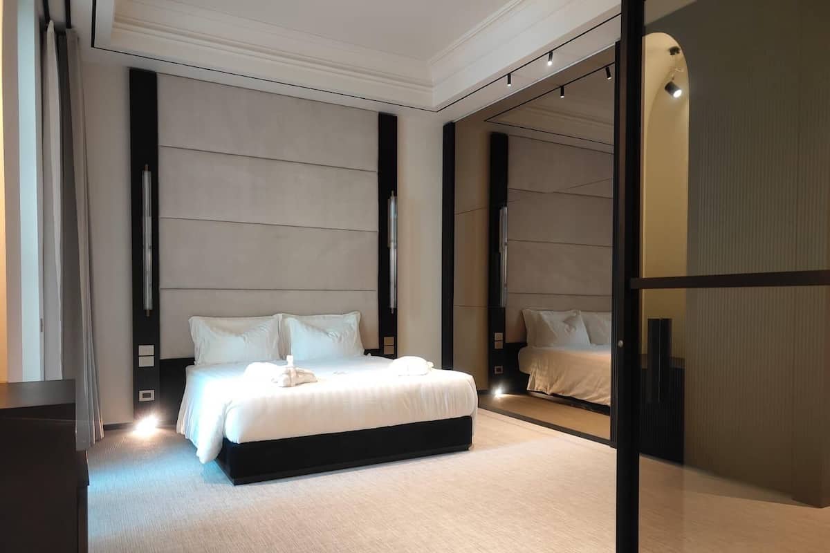 A modern hotel room with a large bed, a mirror, and a view of the cityscape.
