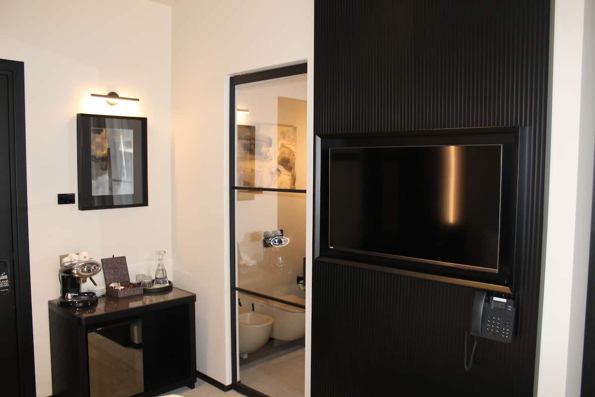 A modern bathroom with a toilet, bidet, and a glass partition. There is a small table with a coffee machine and a telephone.