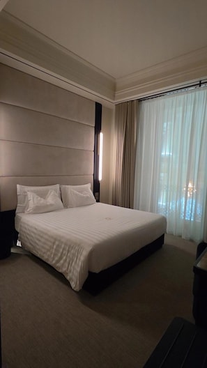 Una habitación de hotel moderna con una cama grande, cabecera, mesita de noche y ventana con cortinas.