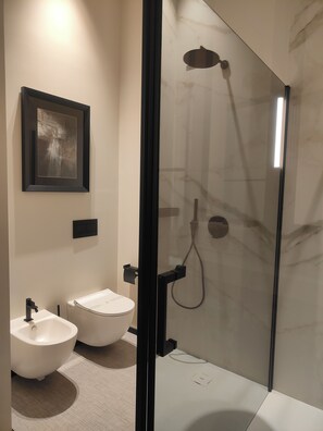 Un baño moderno con ducha de vidrio, dos bidés blancos y una obra de arte abstracta enmarcada en la pared.