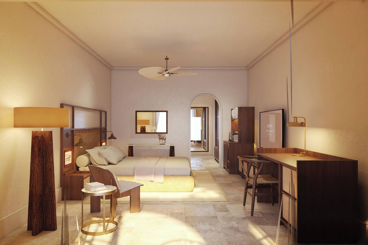 Ein Hotelzimmer mit Bett, Nachttisch, Sessel, Schreibtisch und Deckenventilator.