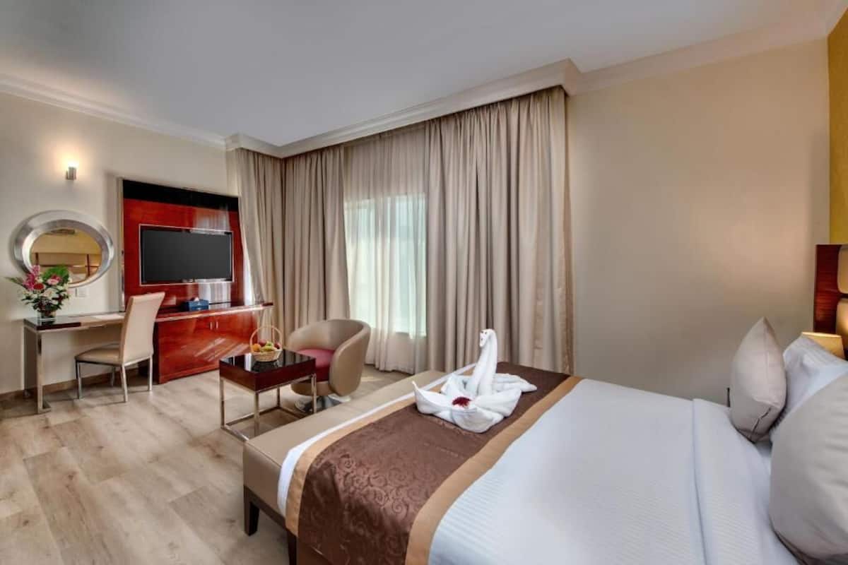A hotel room with a bed, a desk with a chair, a TV, and a large window with curtains.