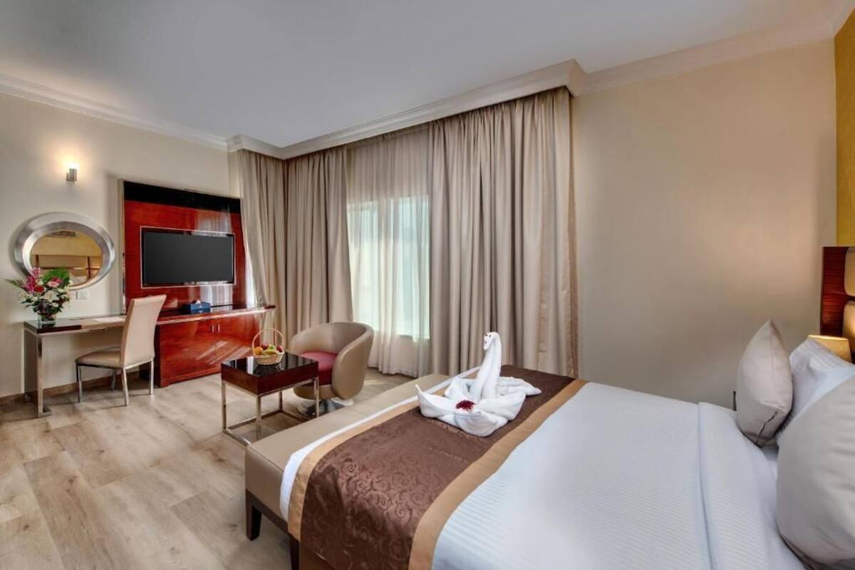 Une chambre d’hôtel avec un lit, un bureau et une chaise, une télévision et une grande fenêtre avec des rideaux.