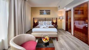 A hotel room with a large bed, a chair, a bedside table with a fruit basket, and a painting on the wall. - City Stay Hotel Expo Center Sharjah (Sharjah)