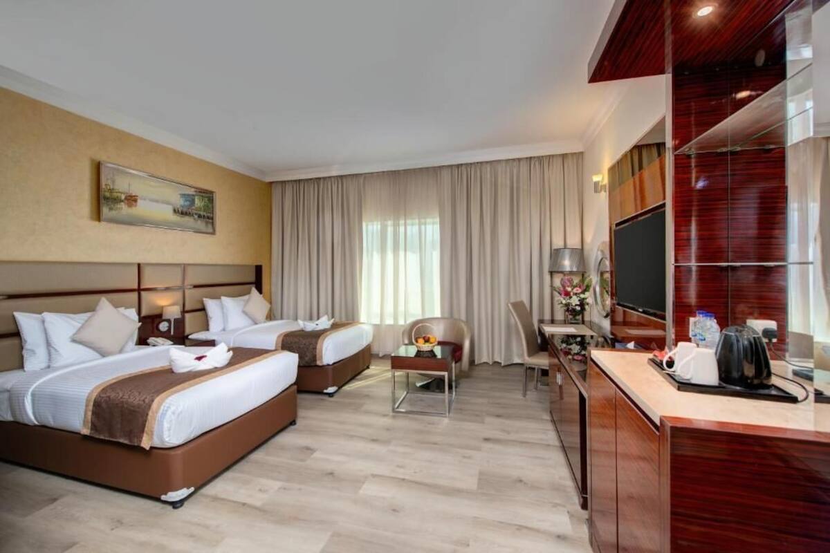 A hotel room with two beds, a desk with a chair, a TV, and a painting on the wall.