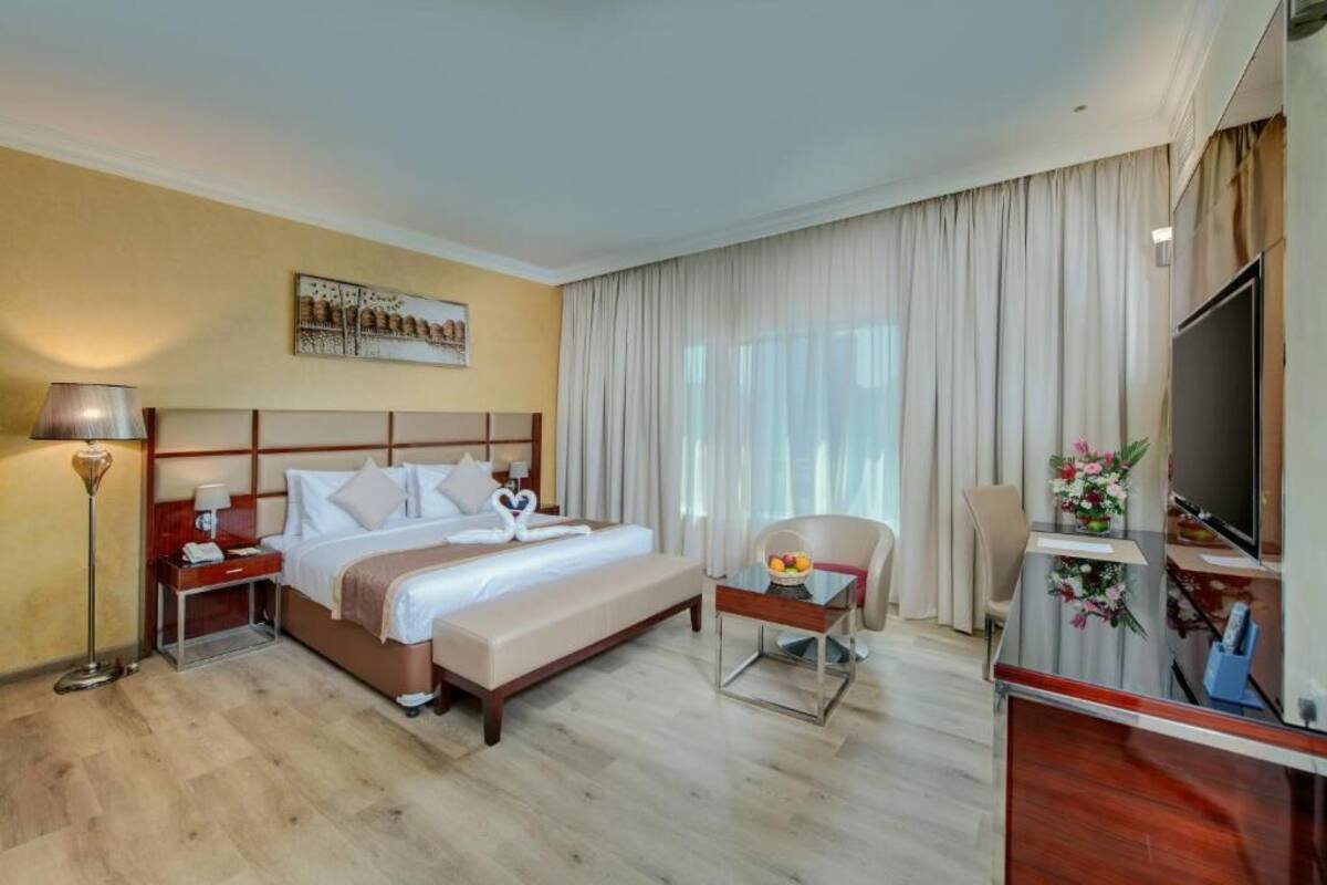 A hotel room with a large bed, a desk, a chair, a TV, and a painting on the wall.
