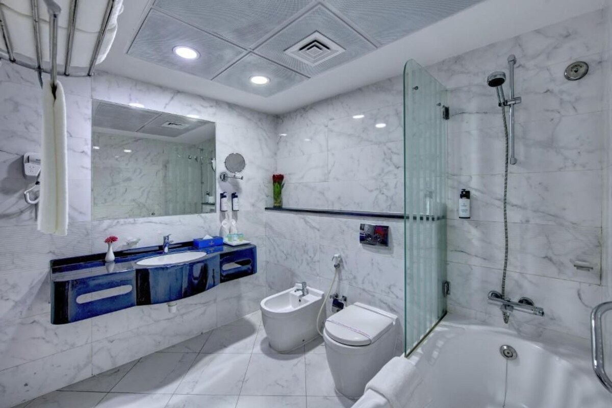 Une salle de bain moderne avec un sol en marbre, une douche en verre, un bidet, des toilettes et un meuble-lavabo avec un miroir et deux vasques.