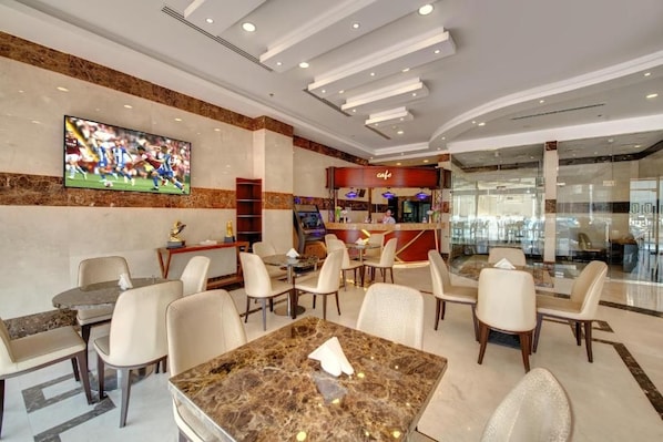 A hotel lobby with marble flooring, leather chairs, a coffee bar, and a large TV screen displaying a soccer match. - City Stay Hotel Expo Center Sharjah (Sharjah)