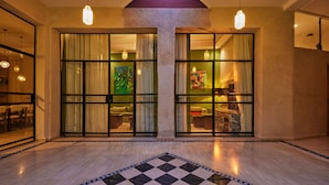 Een hotel lobby met een zwart-wit geruit vloerkleed, grote glazen deuren naar de kamers en hanglampen.