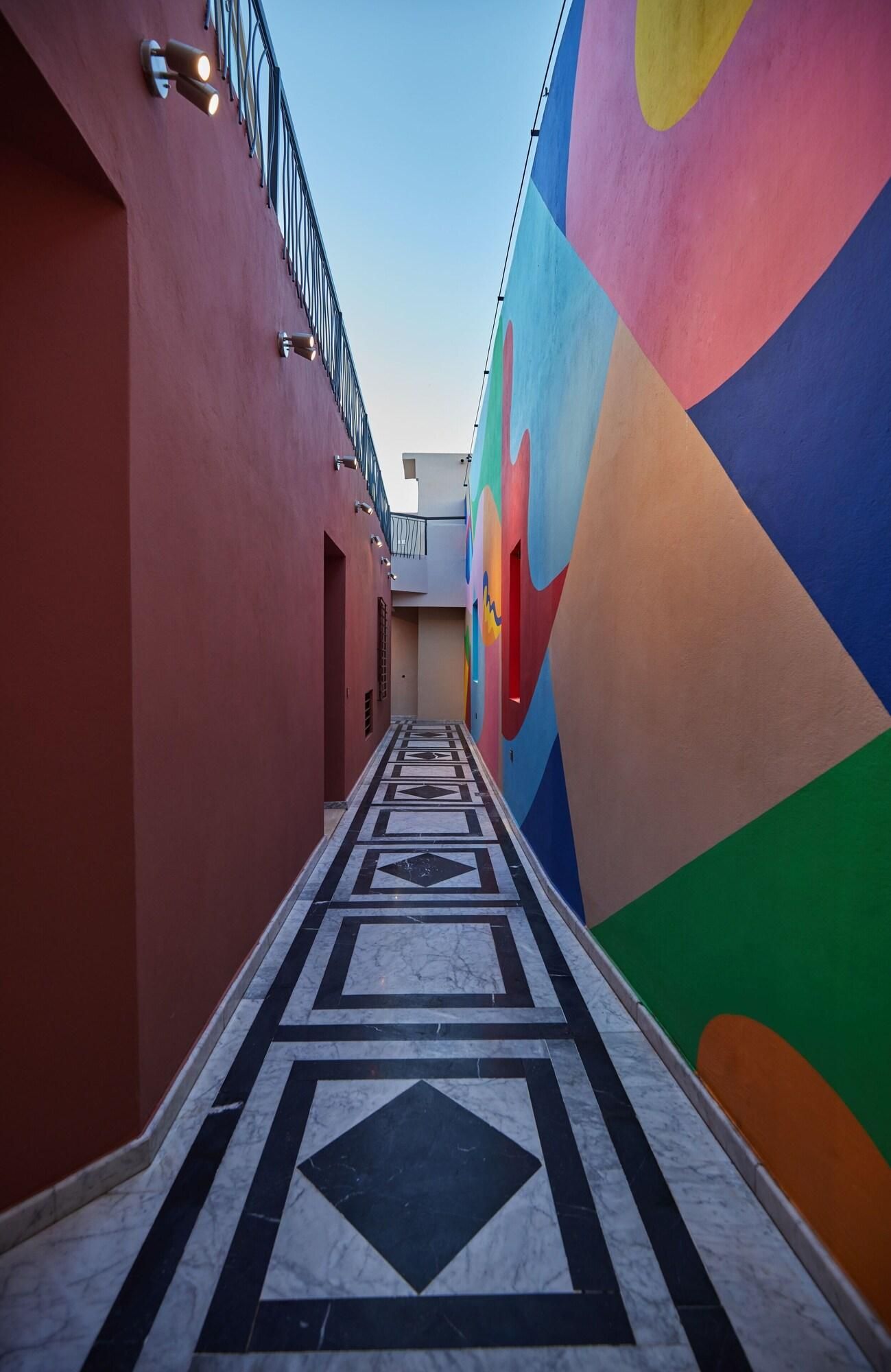Un corridoio con pavimento a motivi geometrici, un murale colorato e una ringhiera metallica a sinistra.