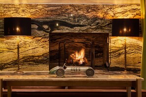 A fireplace with a fire, a vintage car model, and two lamps on a marble wall. - Zen Zone Boutique Riad & Spa (Marrakech)