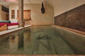 A large indoor pool with a clear 'N' symbol on the floor, wooden benches, and a stone wall with a decorative pattern. - Zen Zone Boutique Riad & Spa (Marrakech)