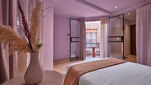 Een slaapkamer met een bed, een vaas met gedroogde planten, een tafel en een balkon met een hekwerk.