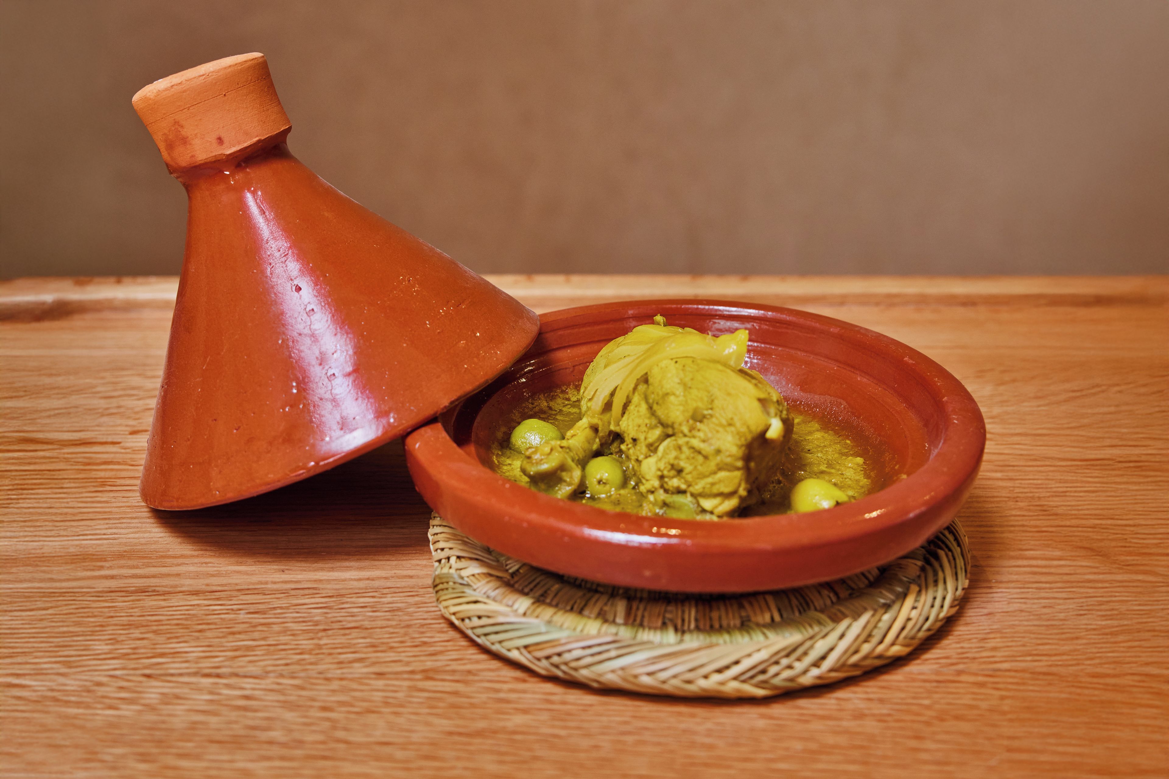 Een traditioneel Marokkaanse tajine, geserveerd in een kleipotje op een geweven mat.