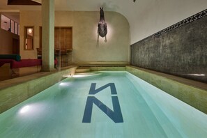 A swimming pool with a large 'N' logo on the floor, a hanging sculpture, and a seating area with a red couch. - Zen Zone Boutique Riad & Spa (Marrakech)