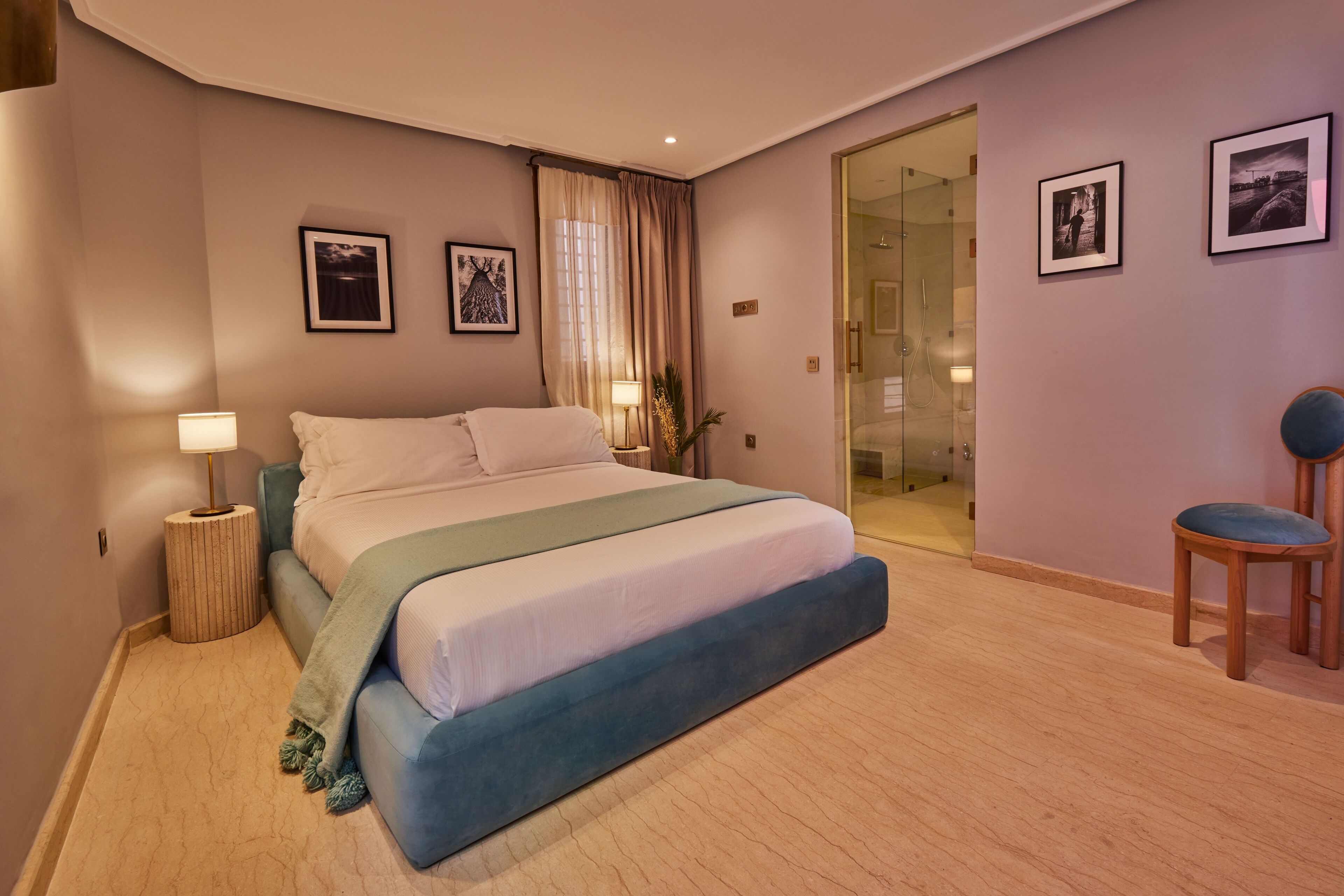 A modern bedroom with a large bed, a glass shower door, and a seating area with a chair.
