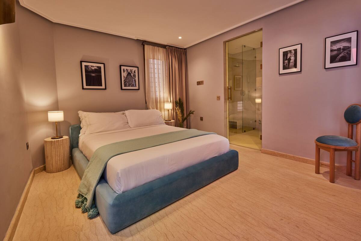 A modern bedroom with a large bed, a glass shower door, and a seating area with a chair.