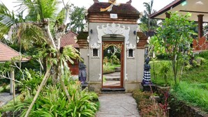 Une porte richement décorée, en bois, entourée d’une végétation luxuriante et de plantes tropicales.