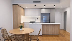 A modern kitchen with a central island, white cabinetry, and a dining area with wicker chairs. - 2BR Aprt West End Hideaway | City Views and Carpark (West End)
