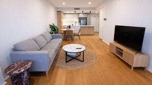 A modern living room with a grey sofa, a marble coffee table, a TV on a wooden stand, and a kitchen in the background. - 2BR Aprt West End Hideaway | City Views and Carpark (West End)