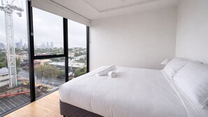 A modern bedroom with a large bed, white linens, and a view of a cityscape through a large window. - 2BR Aprt West End Hideaway | City Views and Carpark (West End)