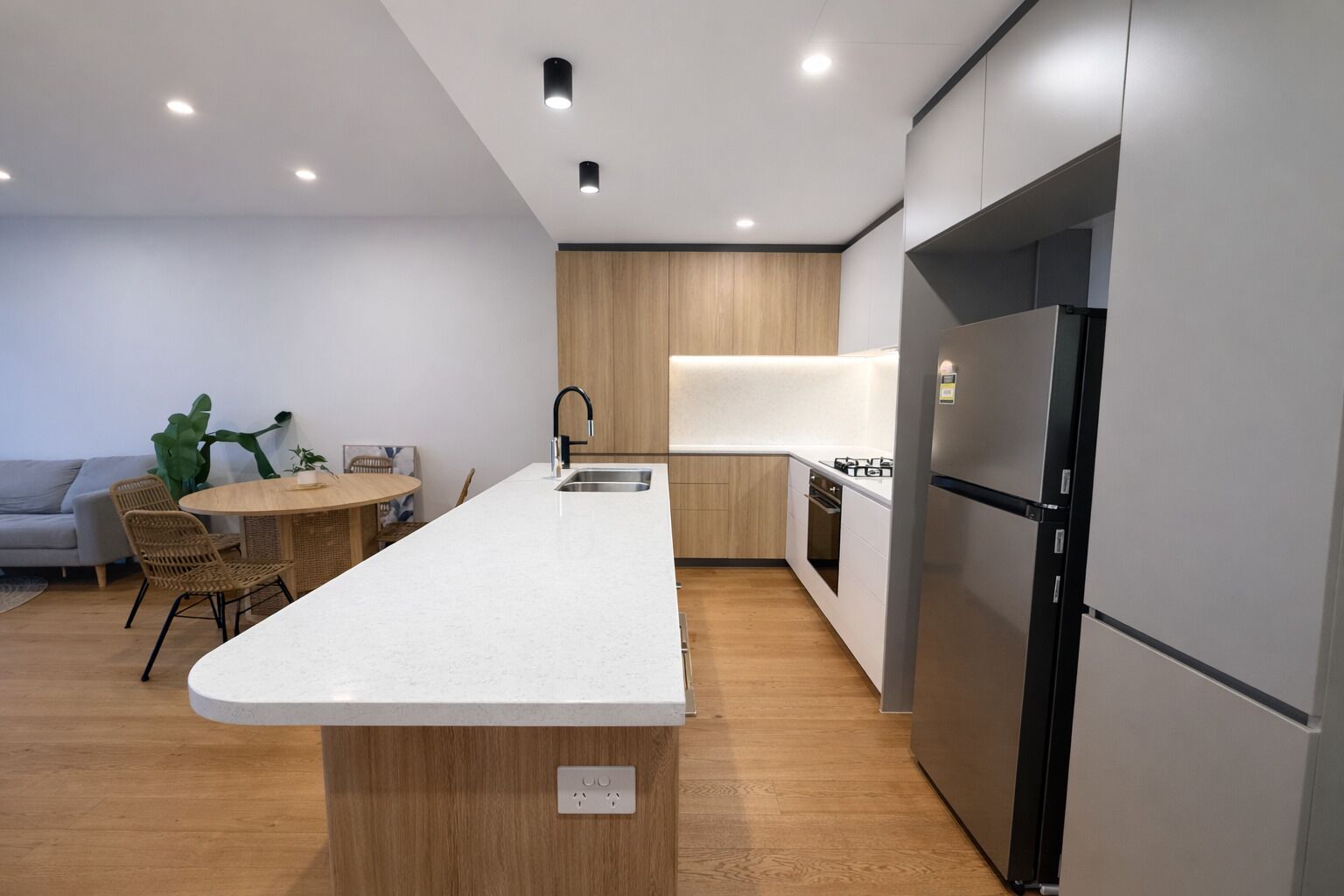 A modern kitchen with a central island, built-in appliances, and a dining area with wicker chairs.