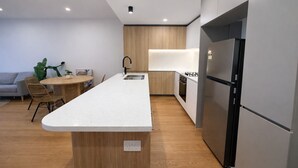 A modern kitchen with a central island, built-in appliances, and a dining area with wicker chairs. - 2BR Aprt West End Hideaway | City Views and Carpark (West End)