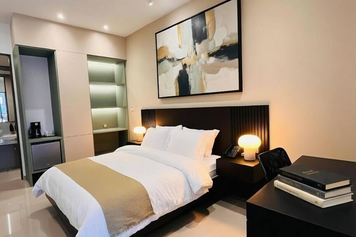 Ein modernes Hotelzimmer mit einem großen Bett, Nachttischen, einem Schreibtisch und einem an der Wand hängenden abstrakten Gemälde.