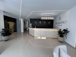 Una moderna recepción con mostrador de mármol, candelabro y un reloj en la pared.