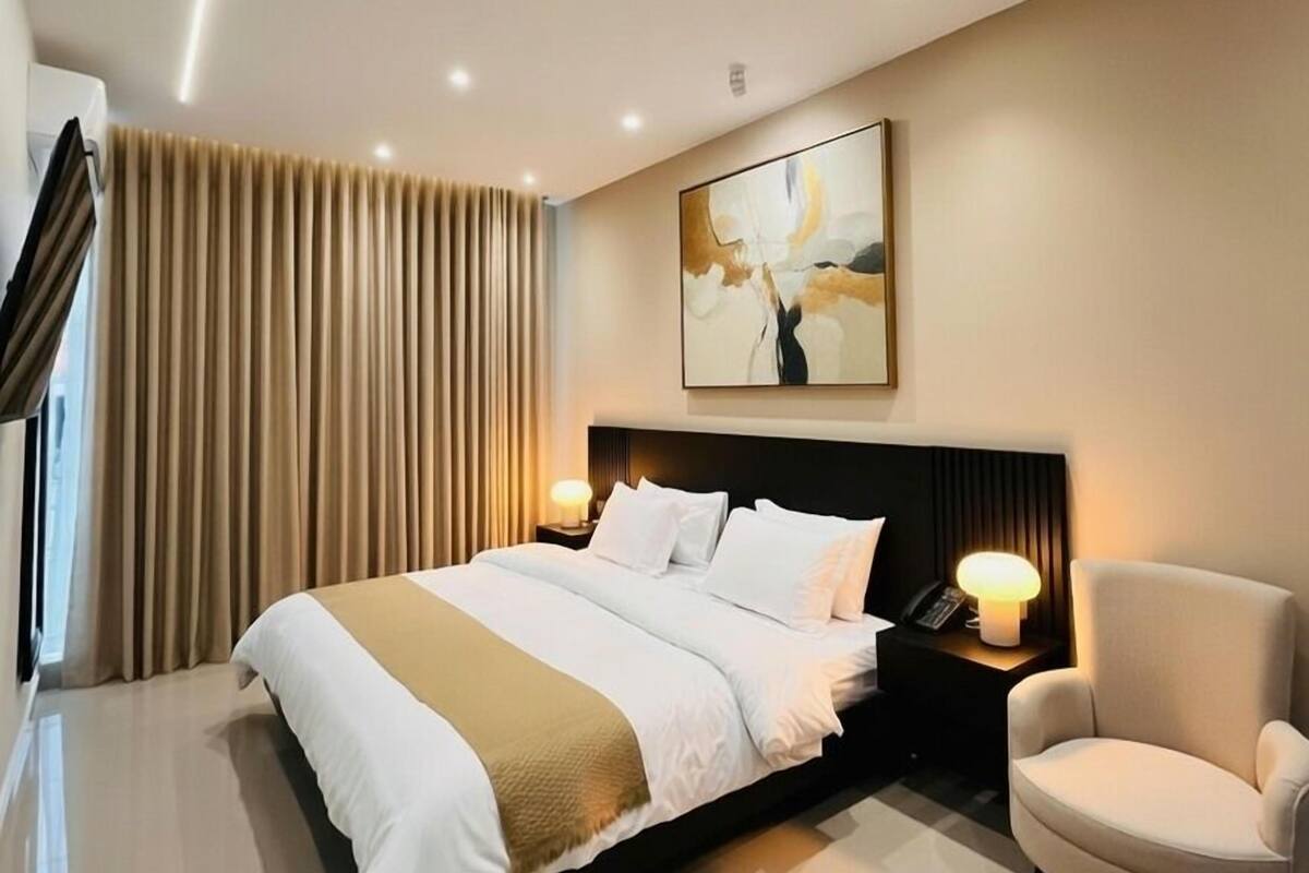 Ein modernes Hotelzimmer mit einem großen Bett, Nachttischlampen, einem Sessel und einem großen abstrakten Gemälde an der Wand.