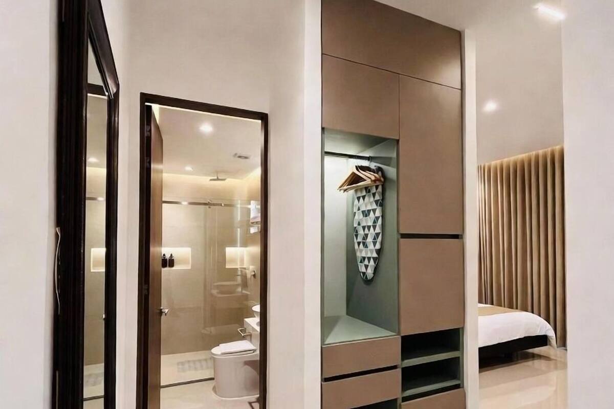Ein modernes Hotelzimmer mit begehbarem Kleiderschrank, einem Bett und einem durch eine offene Tür einsehbaren Badezimmer.