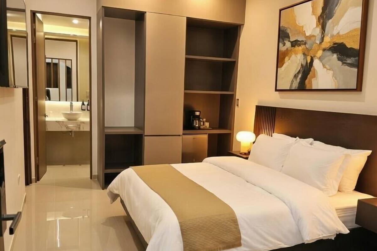 Ein modernes Hotelzimmer mit einem großen Bett, einem Nachttisch mit Lampe, einem Kleiderschrank und einem durchgegangenen Tür sichtbaren Badezimmer.