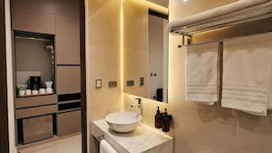 Une salle de bain moderne avec un grand miroir, un lavabo et des toilettes. On trouve un porte-serviettes au-dessus du lavabo, sur lequel est suspendue une serviette.
