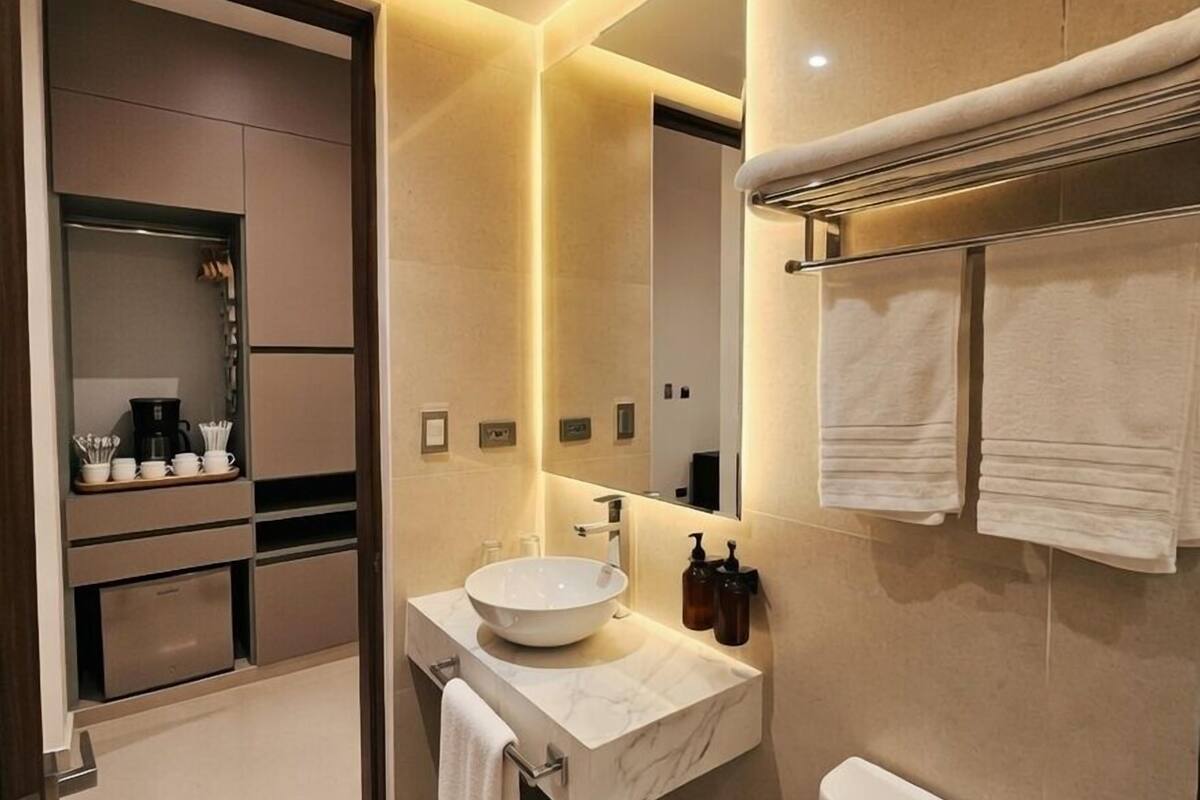 Ein modernes Badezimmer mit einem großen Spiegel, einem Waschbecken und einer Toilette. Über dem Waschbecken befindet sich ein Handtuchhalter, an dem ein Handtuch hängt.